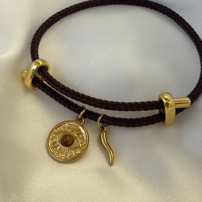 Pulseira de cordão castanho escuro com pendentes dourados sobre tecido branco