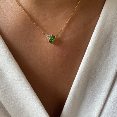 Colar dourado com pendente verde e pedra clara num peito com vestido branco