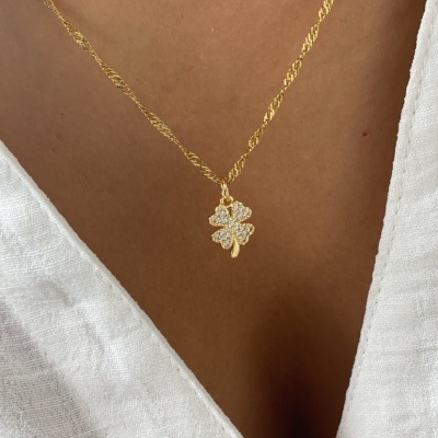 Colar dourado com pingente de trevo cravejado usado com camisa branca