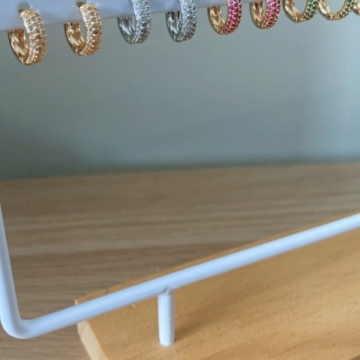 sete pares de brincos argola pequenos com pedras coloridas num suporte branco com base de madeira