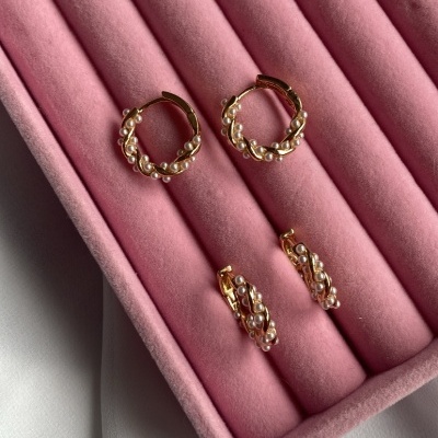 Conjunto de brincos dourados com pérolas numa caixa de veludo rosa.