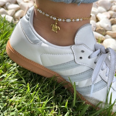 Ténis brancos com sola castanha e bracelete dourada no tornozelo sobre relva