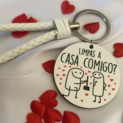 Chaveiro redondo com ilustração e texto em português sobre limpar a casa, com suporte branco e corações vermelhos ao fundo