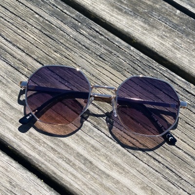 Óculos de sol metálicos com lentes azuis e roxas sobre madeira envelhecida