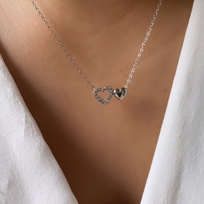 Colar prata com dois corações no pescoço de uma pessoa com camisa branca