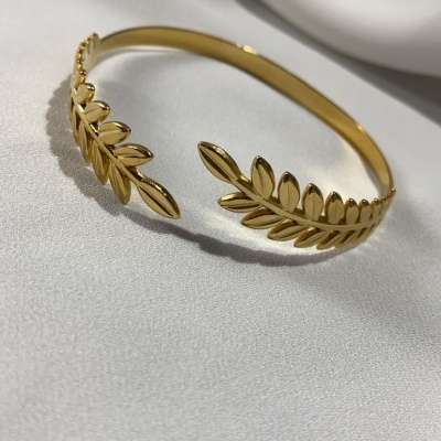 Pulseira rígida dourada com design de folhas em relevo sobre tecido branco