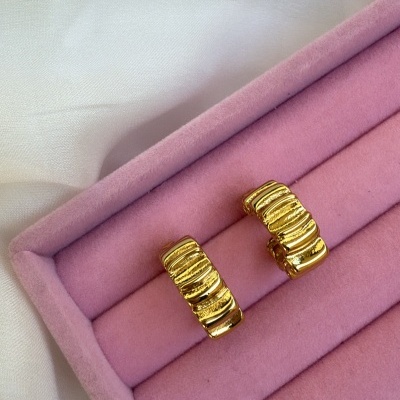 Brincos dourados ondulados numa caixa de veludo rosa