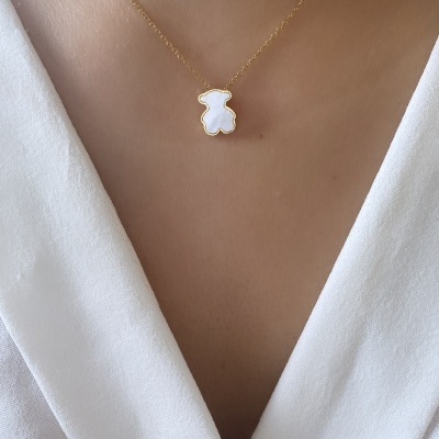 Colar com pendente de urso branco e corrente dourada em pescoço sobre blusa branca