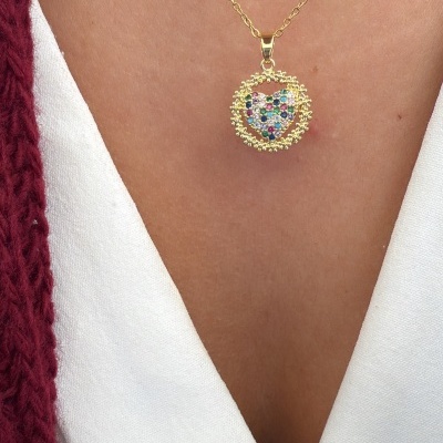 Colar dourado com pendente de coração colorido em fundo branco e cardigan vermelho