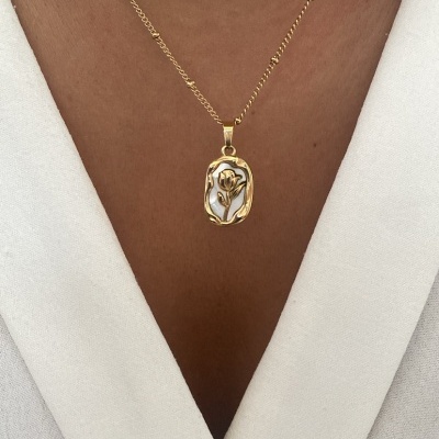 Colar dourado com pendente floral em relevo sobre vestido branco.