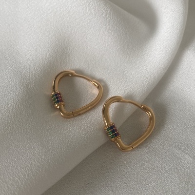 Brincos dourados em forma de coração com pedras coloridas sobre tecido branco