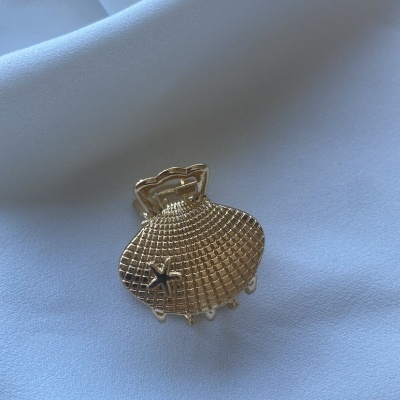 Presilha de cabelo dourada em forma de concha com estrela do mar sobre tecido branco