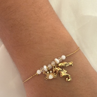 Pulseira dourada com pendentes de mariscos e pérolas no pulso