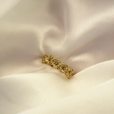 Anel de flores dourado com pedras sobre tecido creme
