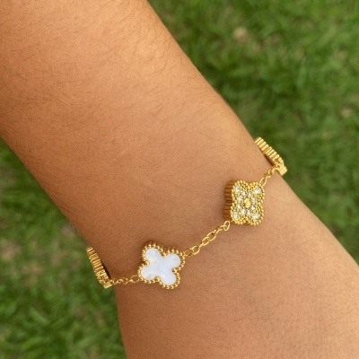 Pulseira dourada com flores branca e dourada com pedras em fundo verde