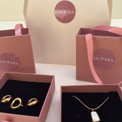 Conjunto de joias douradas com caixas e sacos rosa com logotipo BIJUVERA
