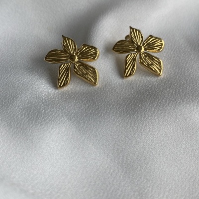 Brincos dourados em forma de flor com quatro pétalas, sobre tecido branco
