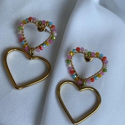 Brincos de coração dourados com contas coloridas sobre tecido branco