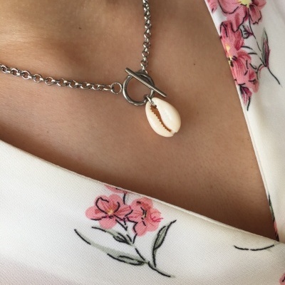 Colar com corrente prateada e pingente de concha sobre roupa branca com flores rosa