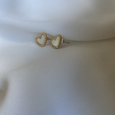 Brincos de coração dourados com interior branco sobre tecido branco.