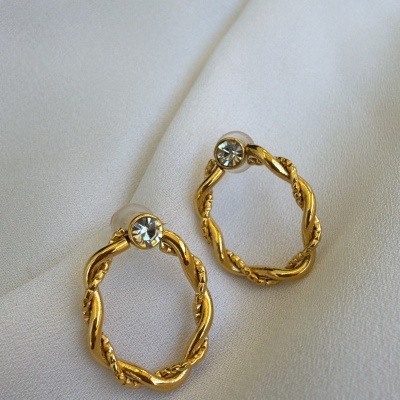 Brincos dourados em forma de argola com pedra brilhante em tecido branco