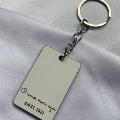 Chaveiro retangular branco com texto em castanho sobre tecido branco
