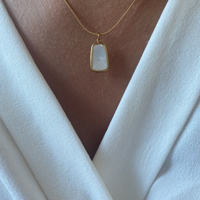 Colar dourado com pendente retangular em madrepérola sobre pele e blusa branca