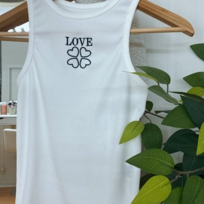 Camisola branca sem mangas com bordado LOVE e corações pendurada em cabide de madeira