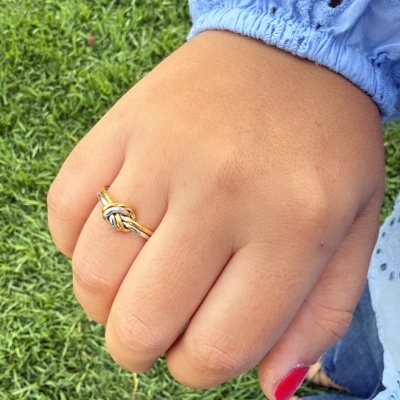 Mão com anel dourado e manga azul clara com bordados na relva