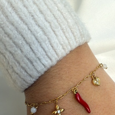 Pulseira dourada com vários pingentes coloridos usada num pulso com manga branca de malha.