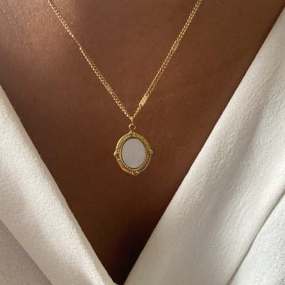 Colar dourado com pendente oval branco em pele morena e camisa branca