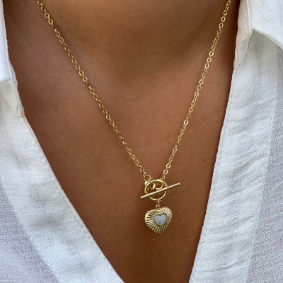 Colar dourado com pendente de coração, usado com camisa branca