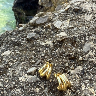 Brincos dourados curvos sobre rochas cinza perto do mar