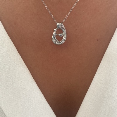 Colar prateado com pendente em forma de gancho, usado com blusa branca