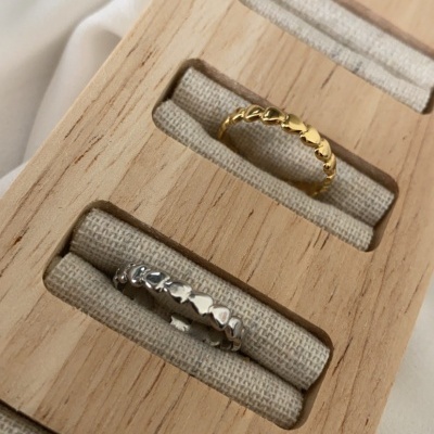 Anéis dourado e prateado com padrão de coração em mostruário de madeira clara com tecido bege