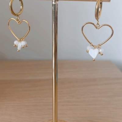 Brincos dourados em forma de coração com pérolas em suporte de madeira