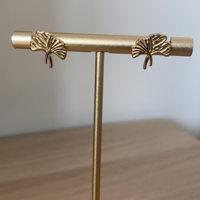 Brincos em metal dourado com formato de folha exibidos num suporte dourado