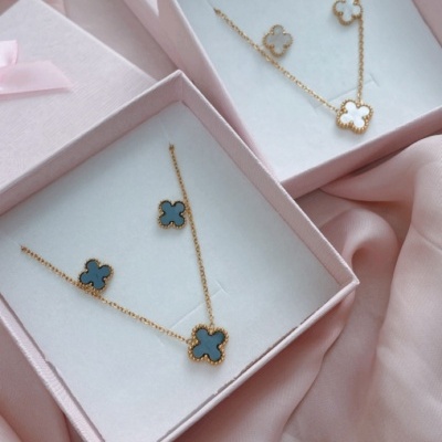 Conjunto de joalharia com colar e brincos em forma de flor azul e branco em caixas com laço cor-de-rosa