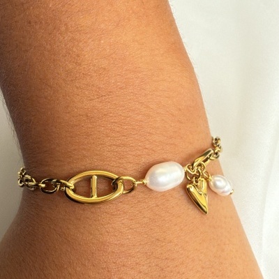 Pulseira dourada com pérolas e pendente de coração num pulso