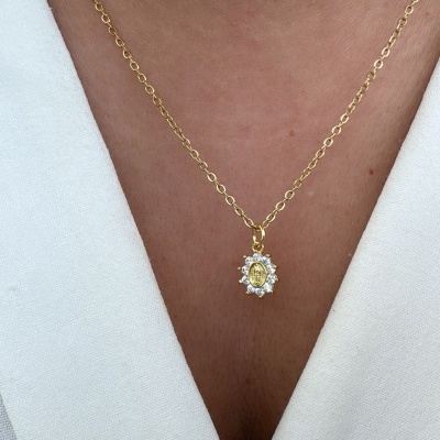 Colar dourado com pendente oval decorado, usado sobre pele e roupa branca