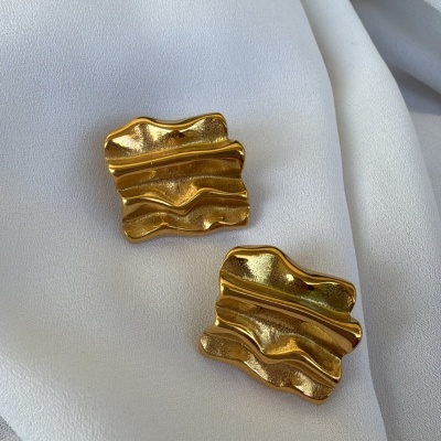 Par de brincos dourados ondulados sobre tecido branco