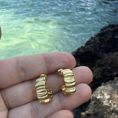 Brincos dourados em relevo segurados à frente do mar e rochas
