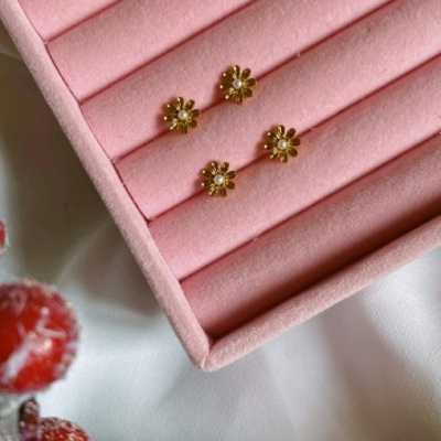 Dois pares de brincos florais dourados com pérolas numa caixa de veludo rosa e decoração natalícia com bagas vermelhas.