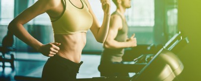 Duas pessoas a correr em passadeiras numa academia com roupa desportiva