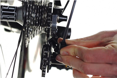 Mão ajustando peça preta perto do cassete de engrenagens de bicicleta