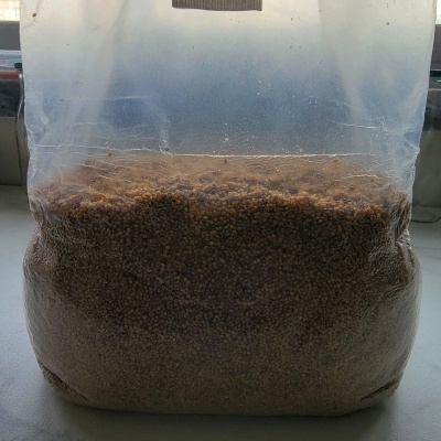 Saco plástico com pequenas pelotas marrons em superfície cinzenta.