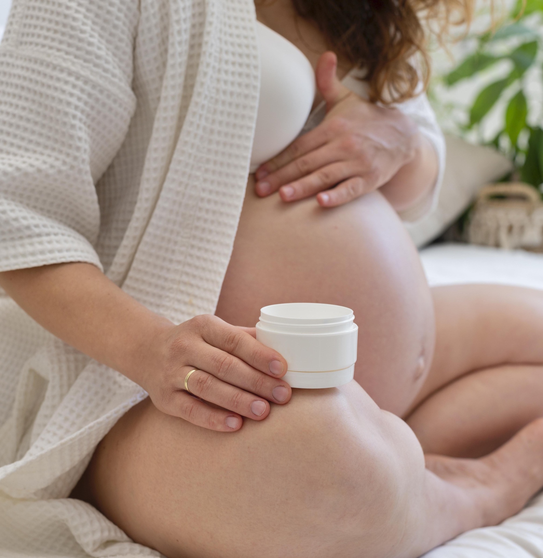 Frasco branco de creme nas mãos de mulher grávida sentada na cama