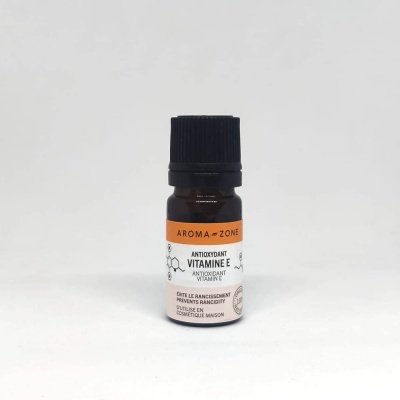 Frasco pequeno de vidro castanho com tampa preta e rótulo branco e laranja de vitamina E antioxidante da Aroma-Zone