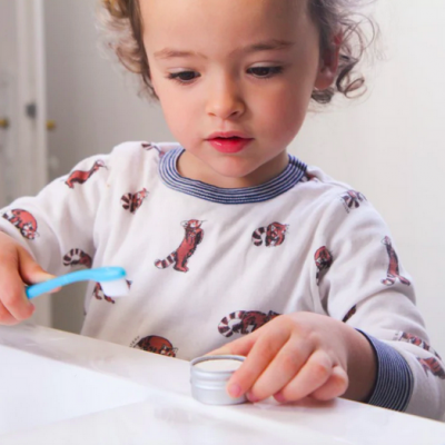 Criança escovando dentes com escova azul e usando camisola com tigrinhos