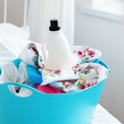 Cesto azul com roupa e garrafa em cama branca